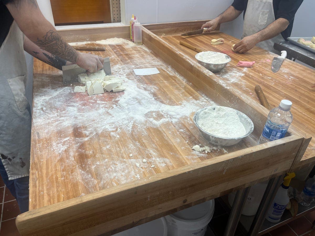 Two bakery workers making dough at a flour-dusted table at Los Portales
